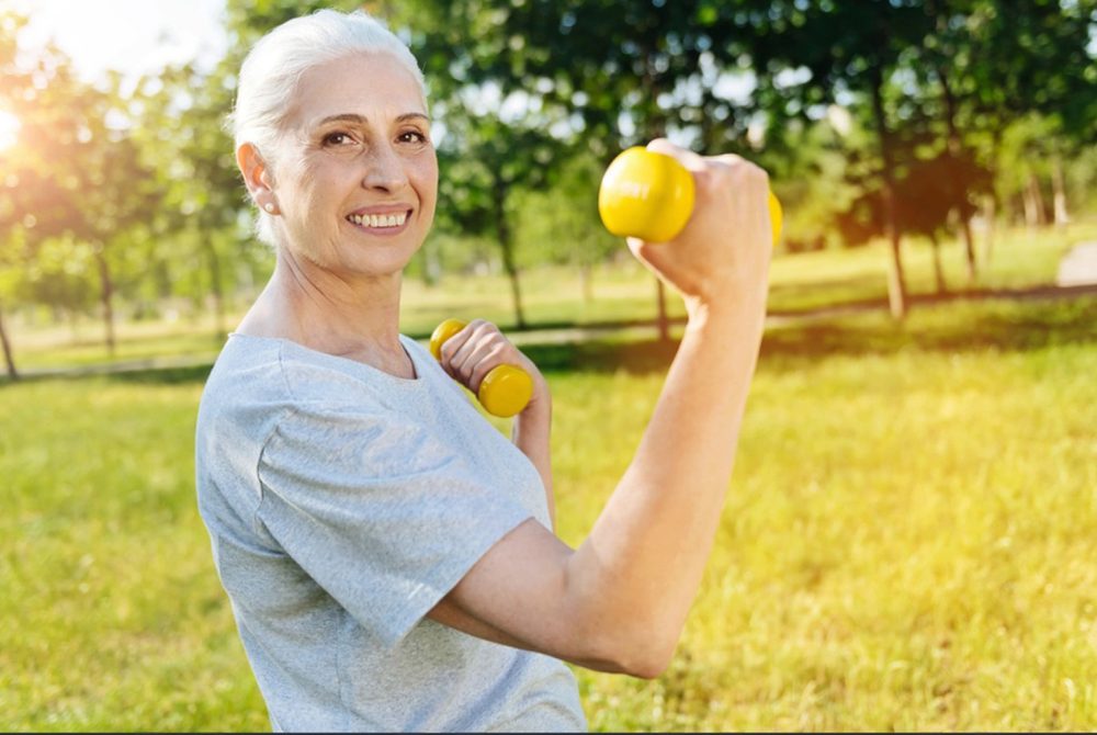 Femme souriante faisant de l’exercice avec des haltères dans un parc